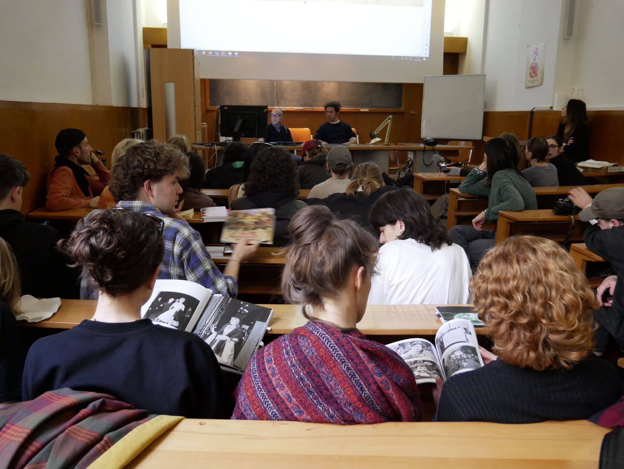 Persone in un'aula universitaria sfogliano dei libri durante una lezione