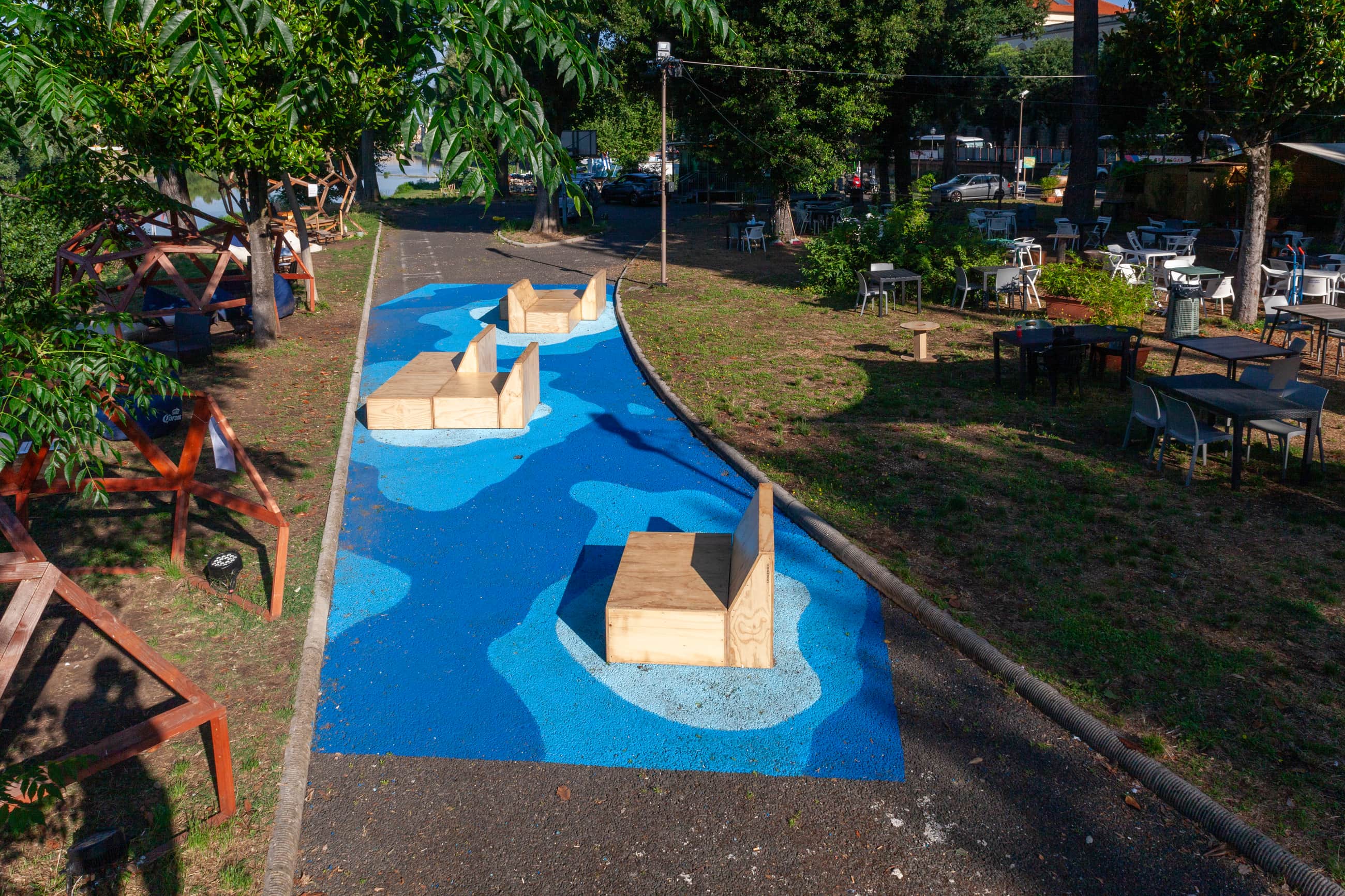 Percorso dipinto in diverse tonalità di blu con sedute in legno, lungo un'area alberata