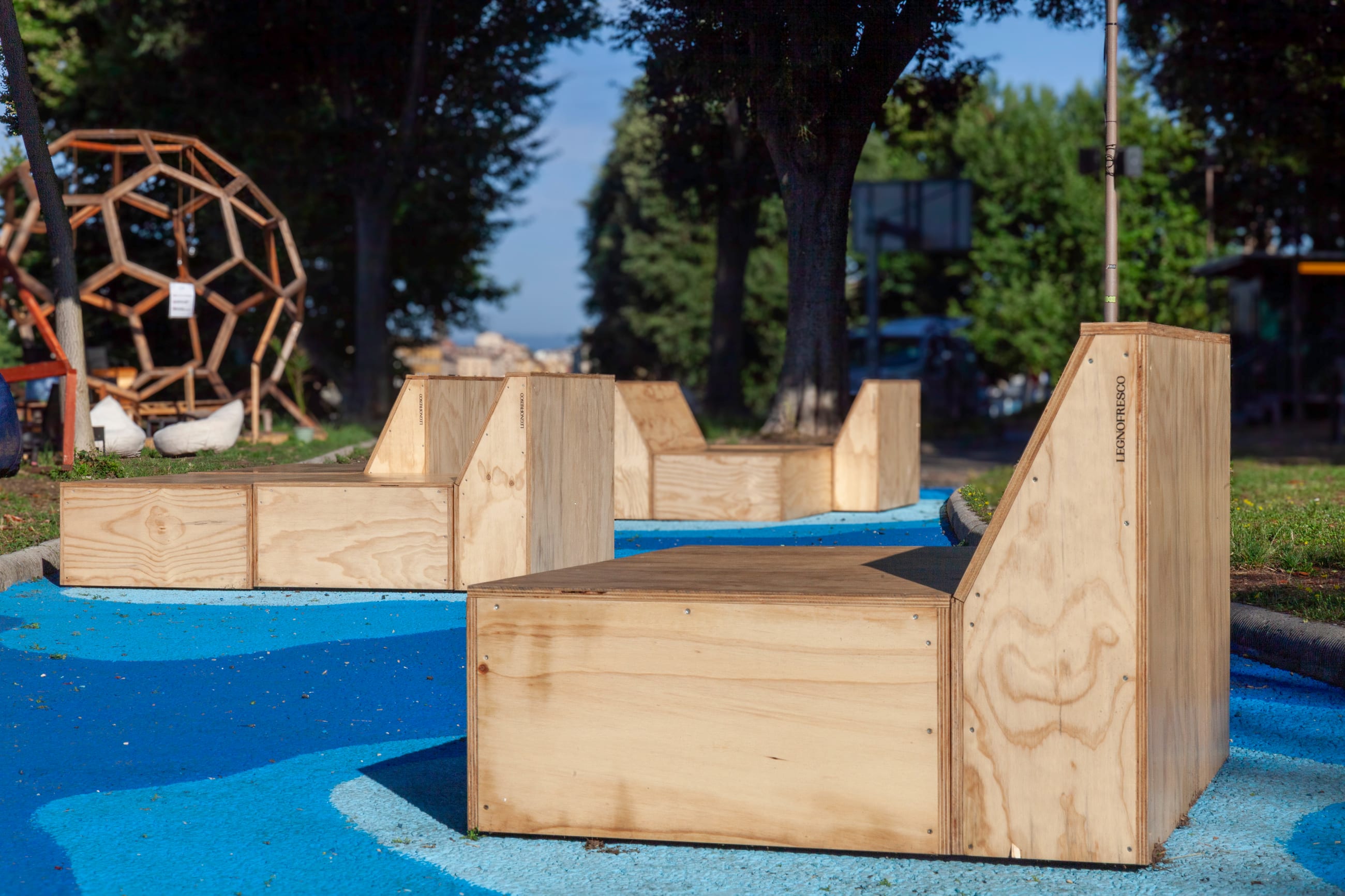 Sedute in legno su pavimentazione blu, con una cupola in legno sullo sfondo