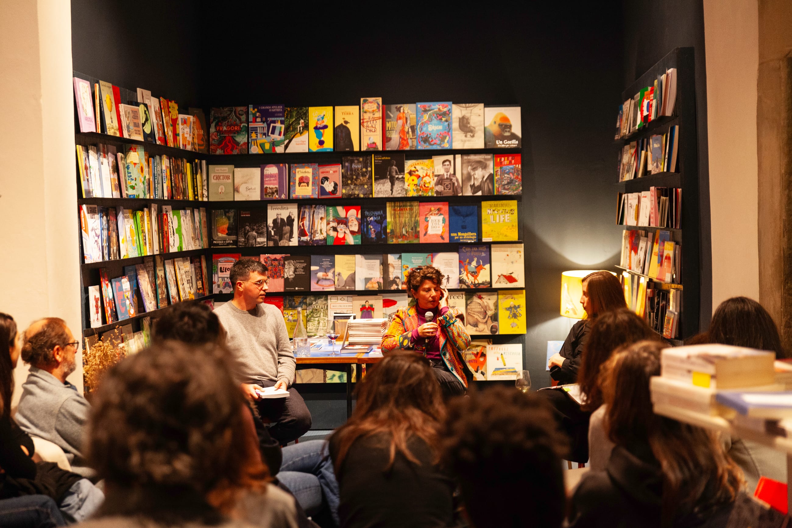 Pubblico seduto in una libreria mentre una persona interviene al microfono