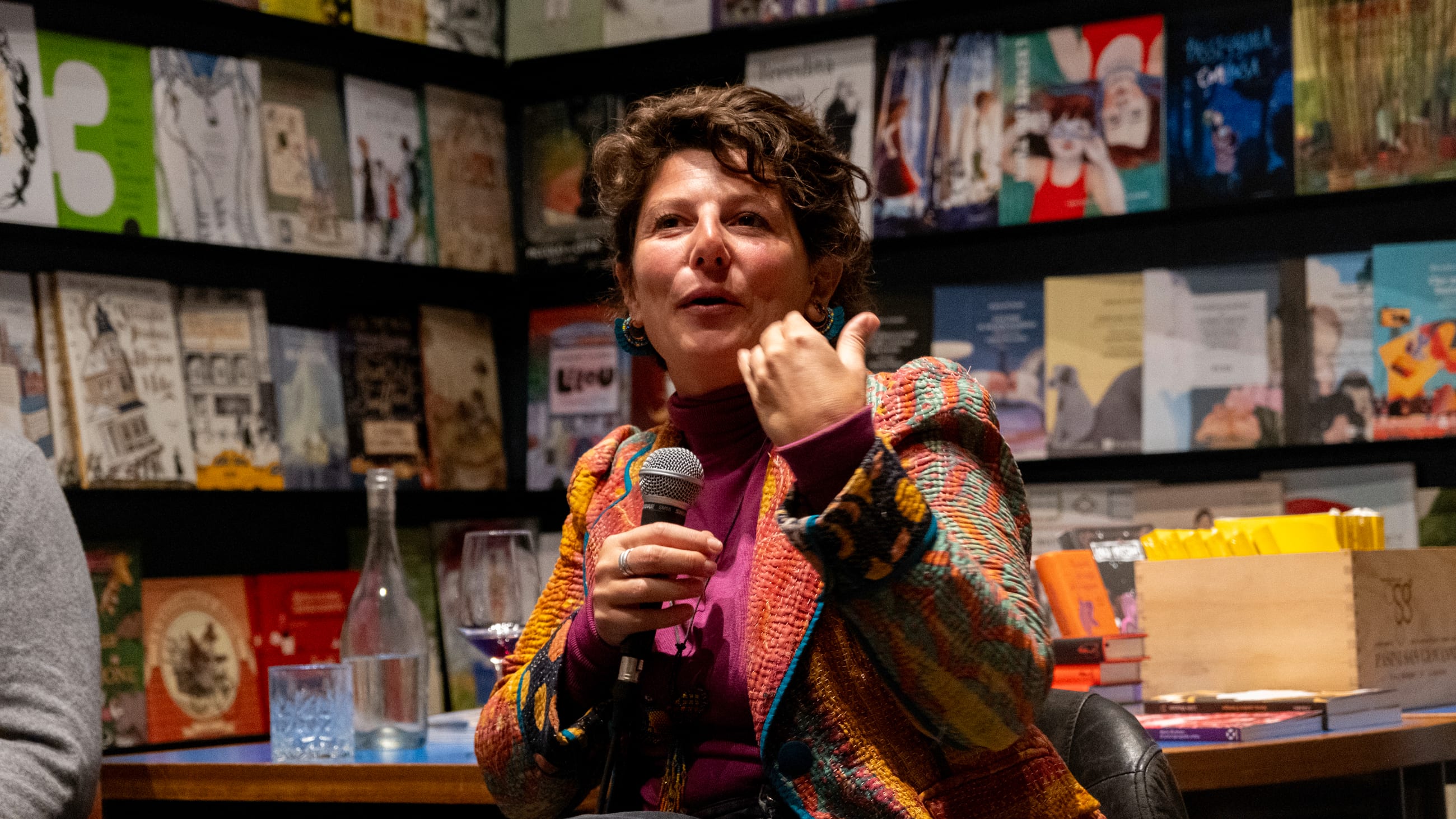 Persona parla al microfono seduta davanti a scaffali di libri illustrati