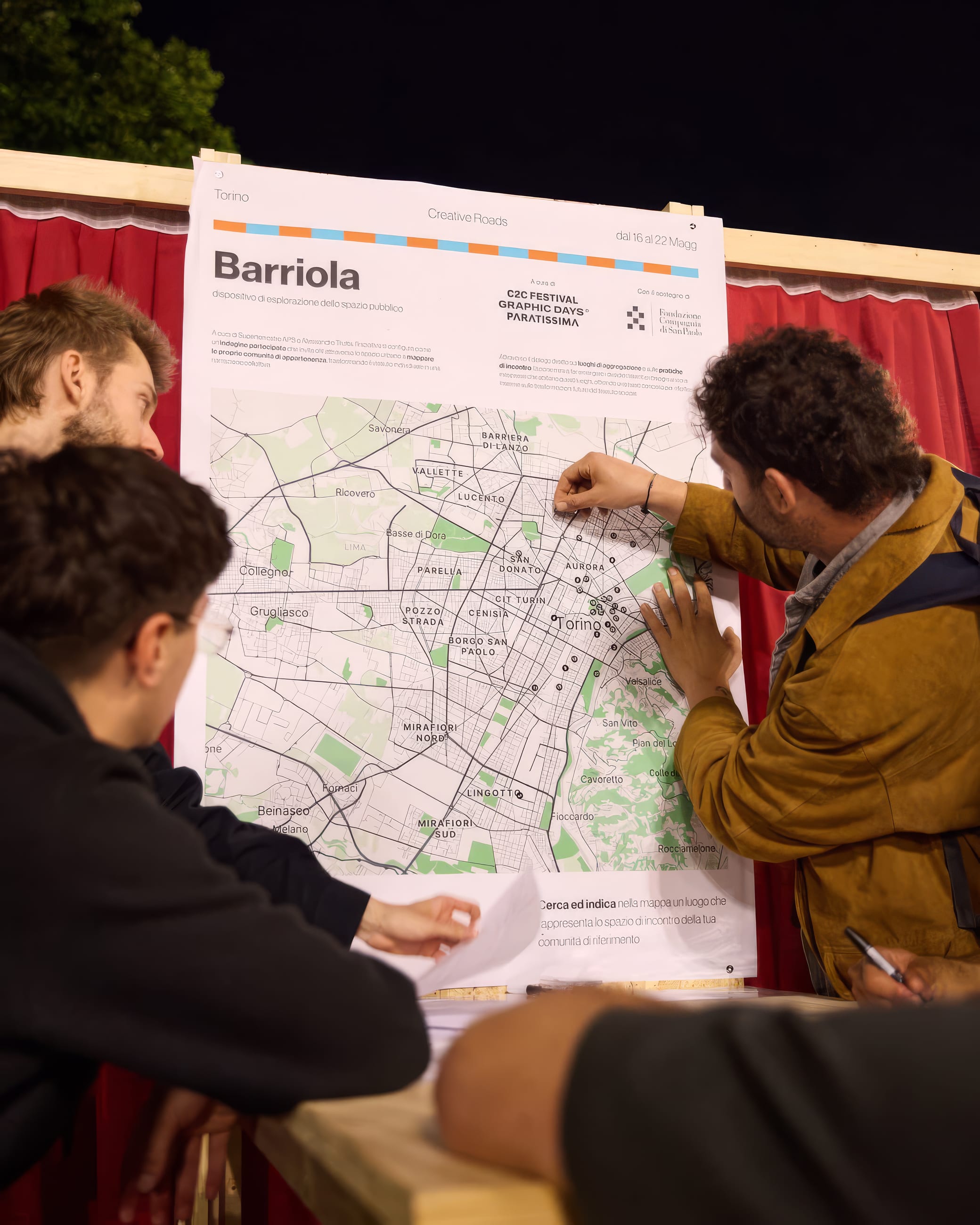 Persone discutono di sera davanti a un pannello con la mappa di un quartiere