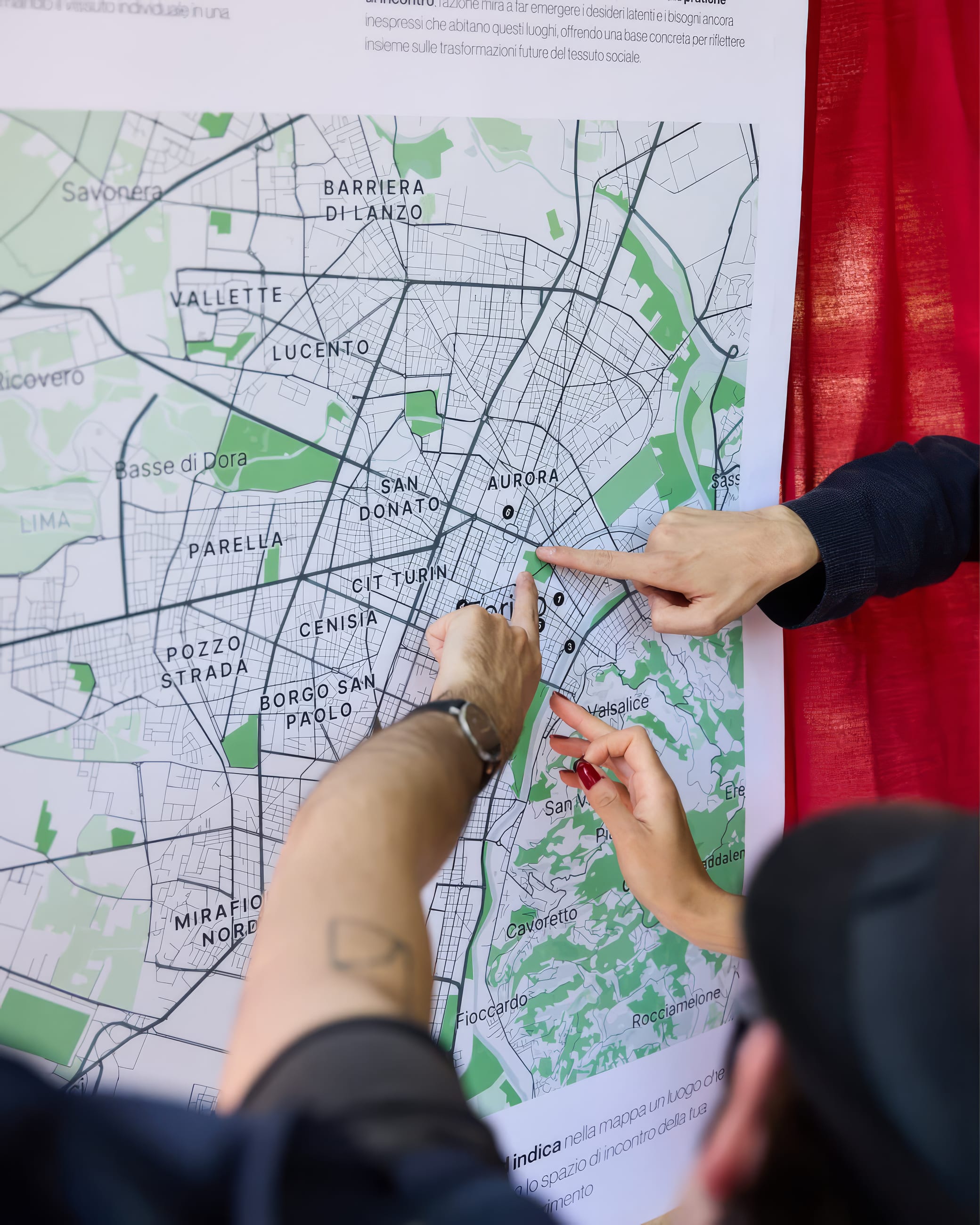 Mani indicano dei punti su una grande mappa della città appesa a una tenda rossa