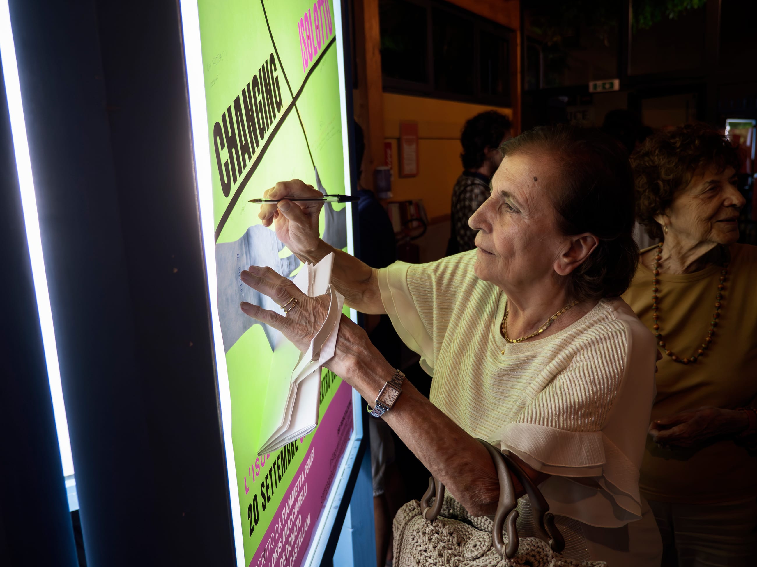 Persona scrive su un poster luminoso verde mentre un'altra la osserva