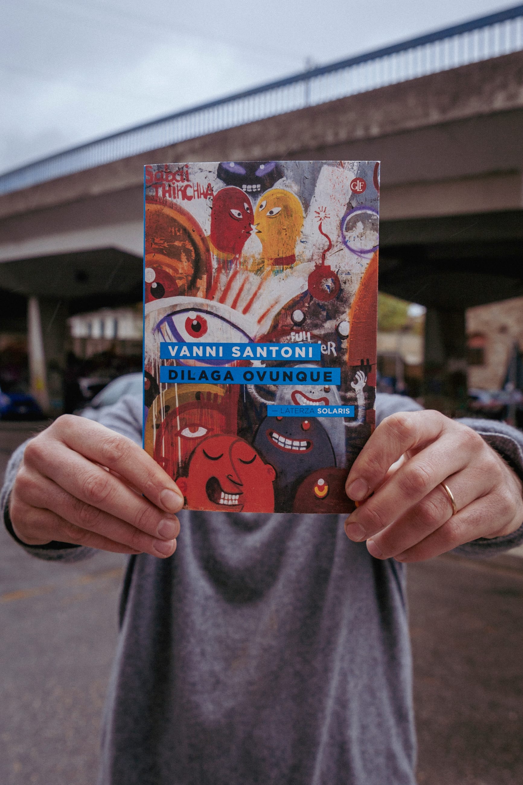 Persona regge davanti a sé un libro dalla copertina illustrata, sotto un cavalcavia