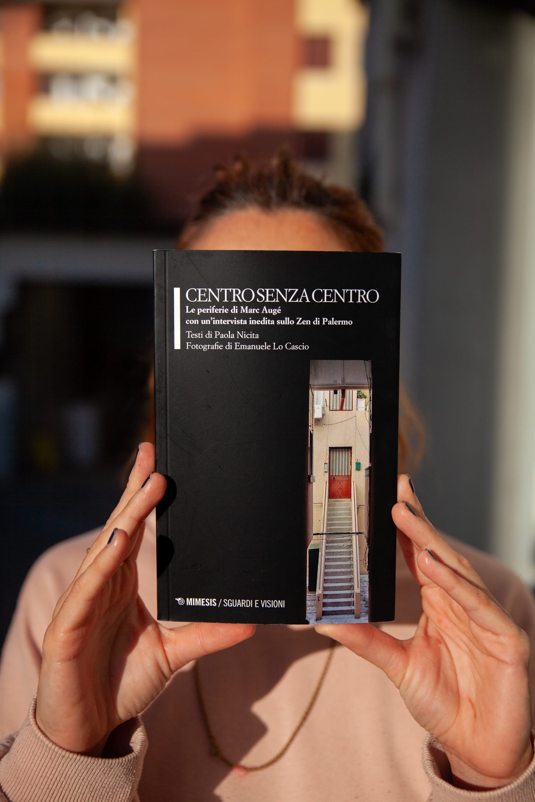 Mani reggono davanti al volto un libro nero con una scala fotografata in copertina