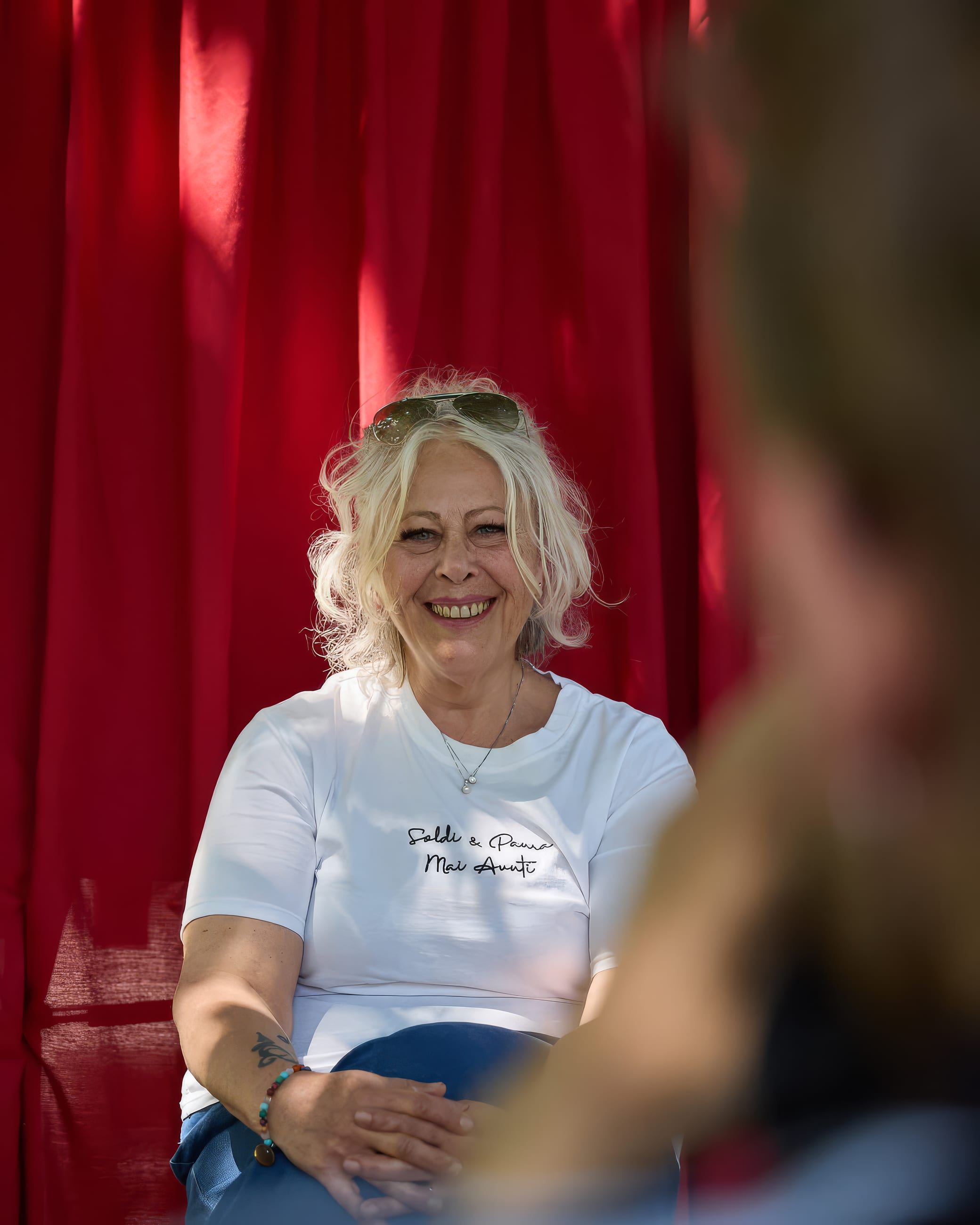 Persona sorridente seduta davanti a una tenda rossa, durante una conversazione