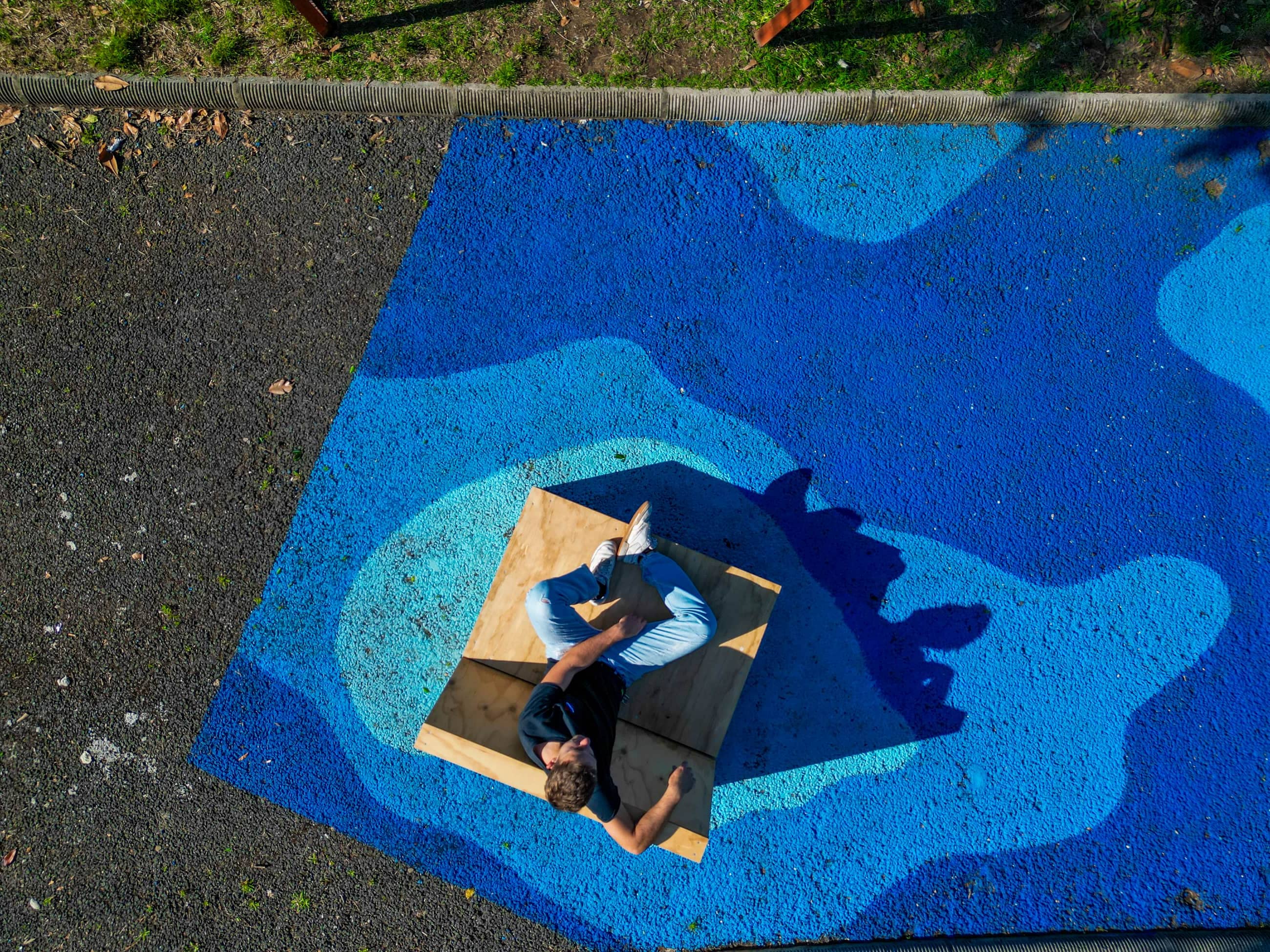 Vista dall'alto di una persona sdraiata su una seduta in legno al centro di forme blu