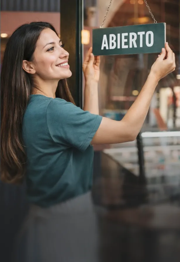 Mujer sonriente colgando un cartel de abierto en la entrada de una tienda.