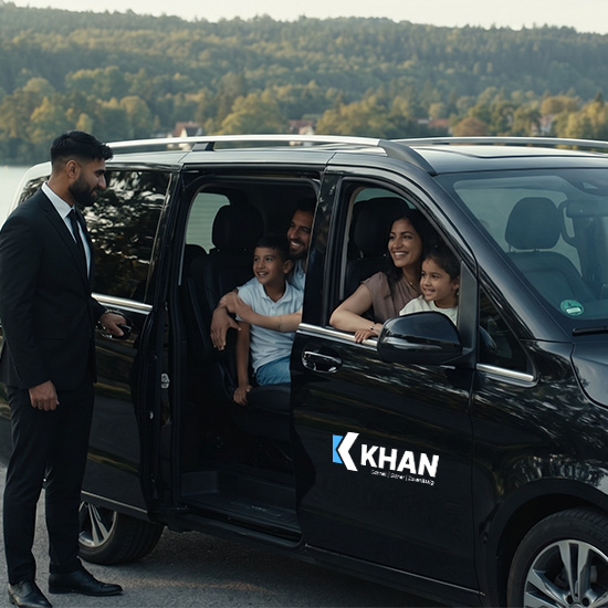 Familie mit zwei Kindern sitzt lächelnd in einem schwarzen Van mit offener Tür, während ein Mann im Anzug neben dem Fahrzeug steht. KHAN Fahrdienst Konstanz und Überlingen