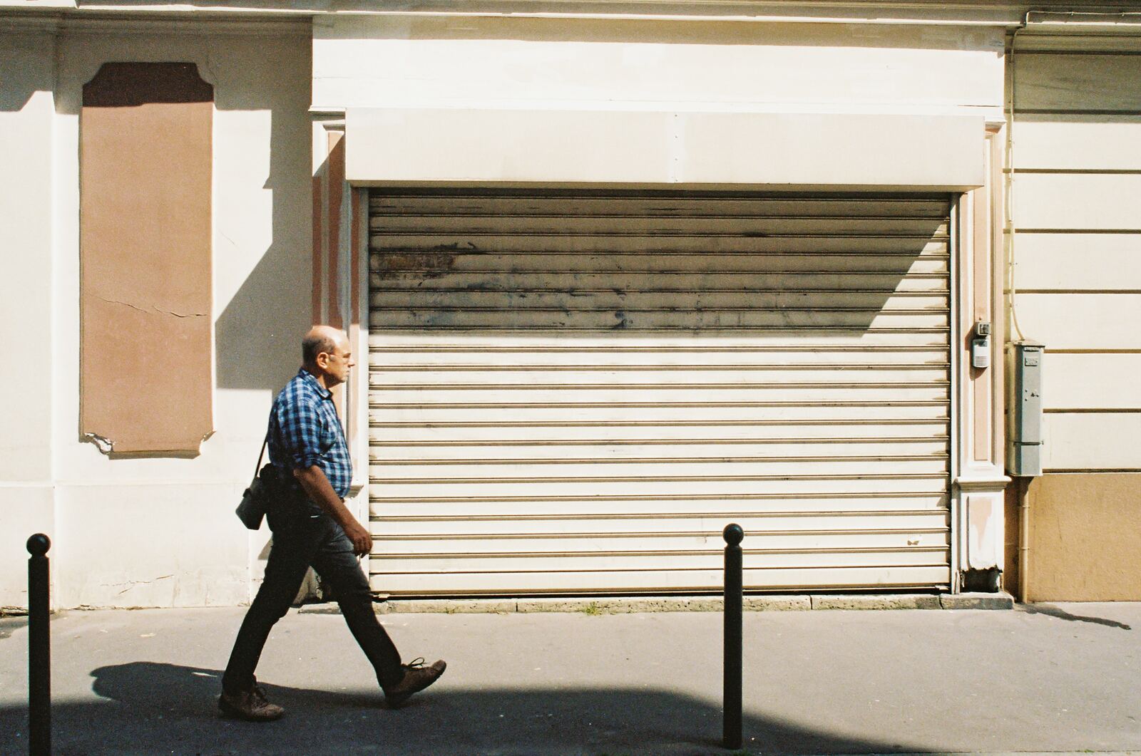 man in blue and white plaid dress shirt and black pants standing near white roll up
