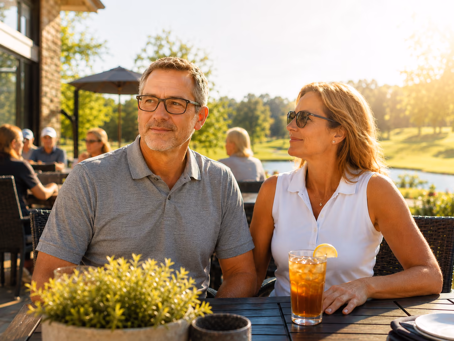 A couple seated at an outside restaurant table on a sunny day while the woman enjoys an iced tea