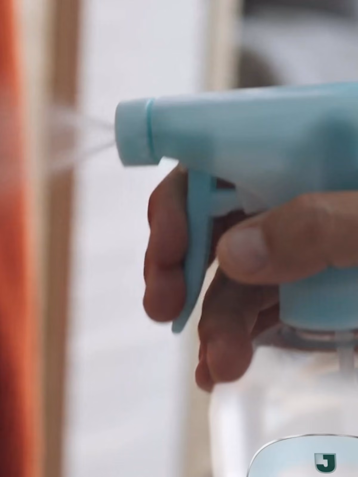 Mão segurando um borrifador azul claro que está soltando spray branco.