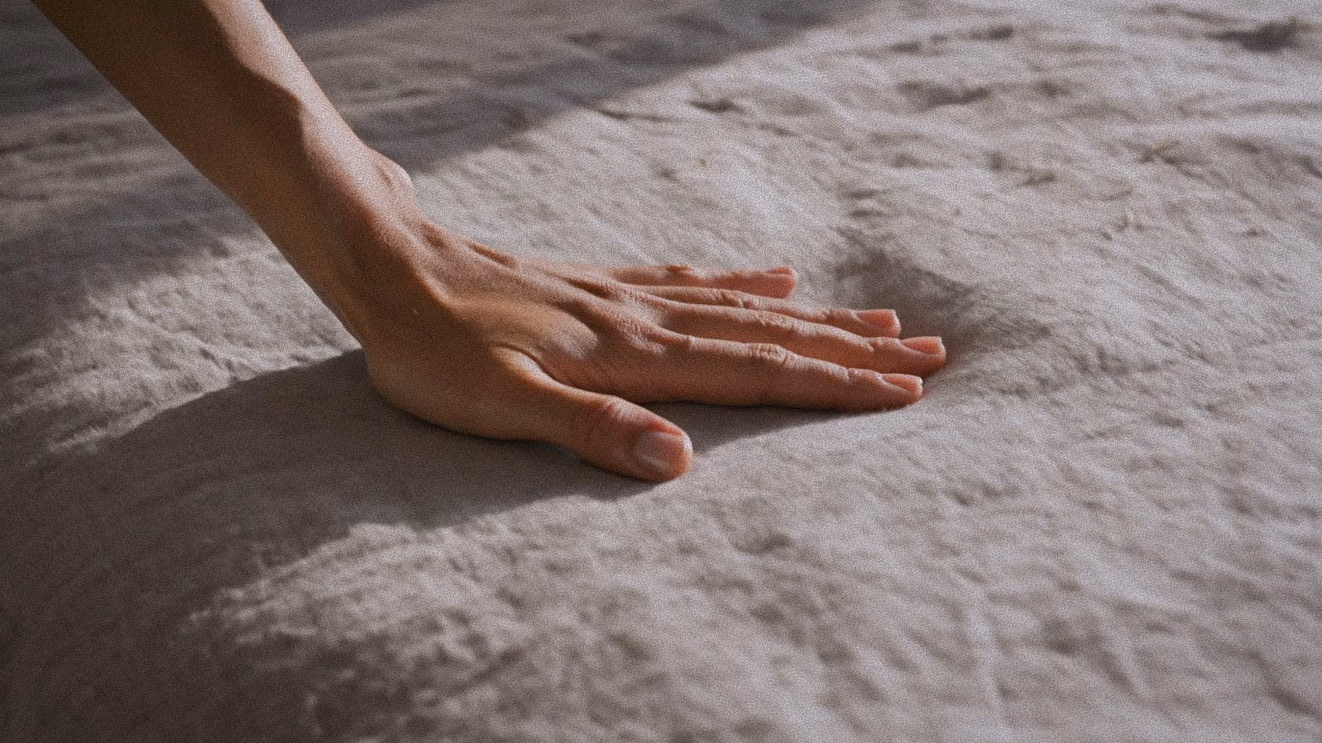 Mão humana descansando sobre um tecido cinza macio com textura visível.