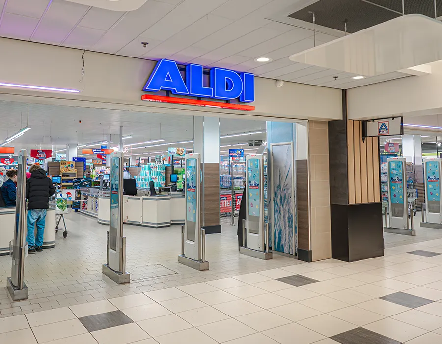 Ingang van Aldi in een winkelcentrum met blauw verlicht logo en beveiligingspoortjes