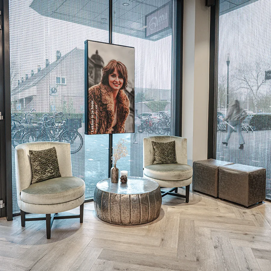 Sfeervolle wachtruimte bij Ami Kappers in Winkelcentrum Hasselo Hengelo met fluwelen fauteuils, ronde salontafel en digitaal beeldscherm