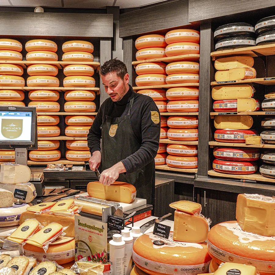 Medewerker snijdt kaas bij Patrick’s in Winkelcentrum Hasselo tussen grote kazen