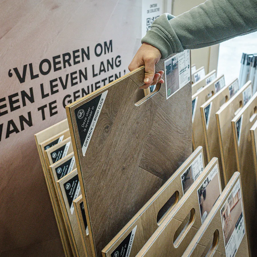 Hand pakt vloerstaal uit display bij Picobello Vloeren in Winkelcentrum Hasselo