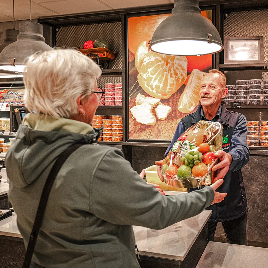 Medewerker overhandigt fruitmand aan klant bij Eddy Weegink
