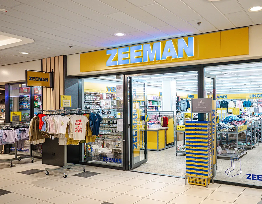 Ingang van Zeeman in Winkelcentrum Hasselo met het gele logo, kledingrekken buiten en een blik in de winkel met afdelingen Verzorging en Lingerie