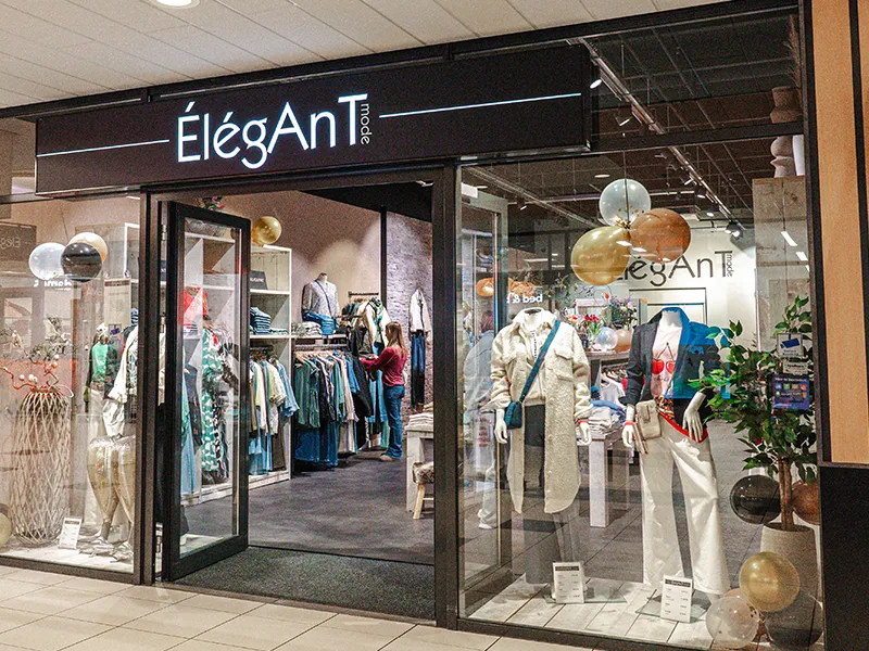 Ingang van ÉlégAnT Mode in Winkelcentrum Hasselo met zwarte gevel, verlichte etalage met mannequins en gouden ballonnen