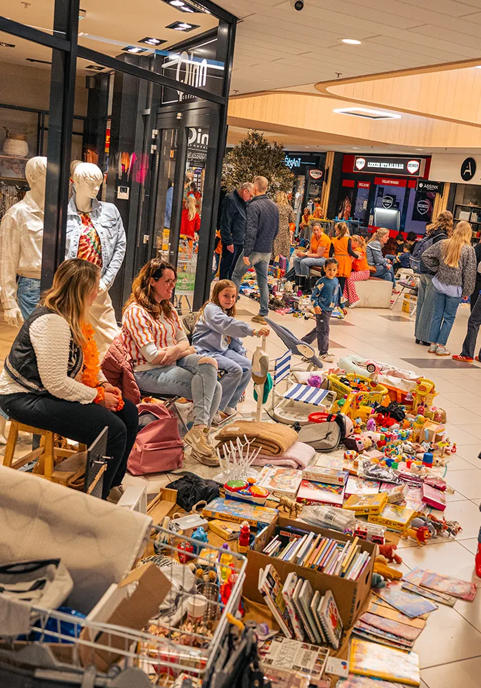 Kinderen en ouders bij een kleedjesmarkt in Winkelcentrum Hasselo met speelgoed, boeken en spellen uitgestald op de grond