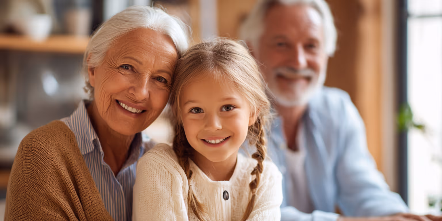 Smiling elderly woman and young girl with braided hair posing closely, with a smiling older man in the background.