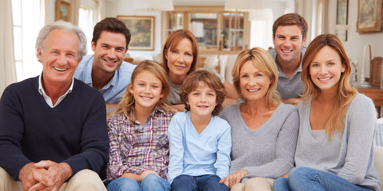 Three generations of a smiling family, including two children seated in front with adults behind them, in a warmly lit living room.