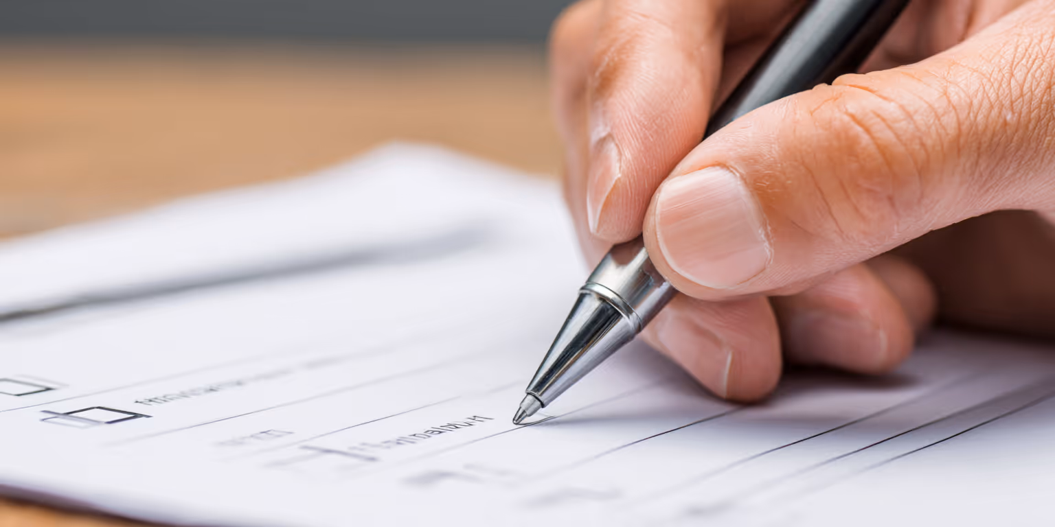 Close-up of a hand holding a pen and filling out a form on paper.
