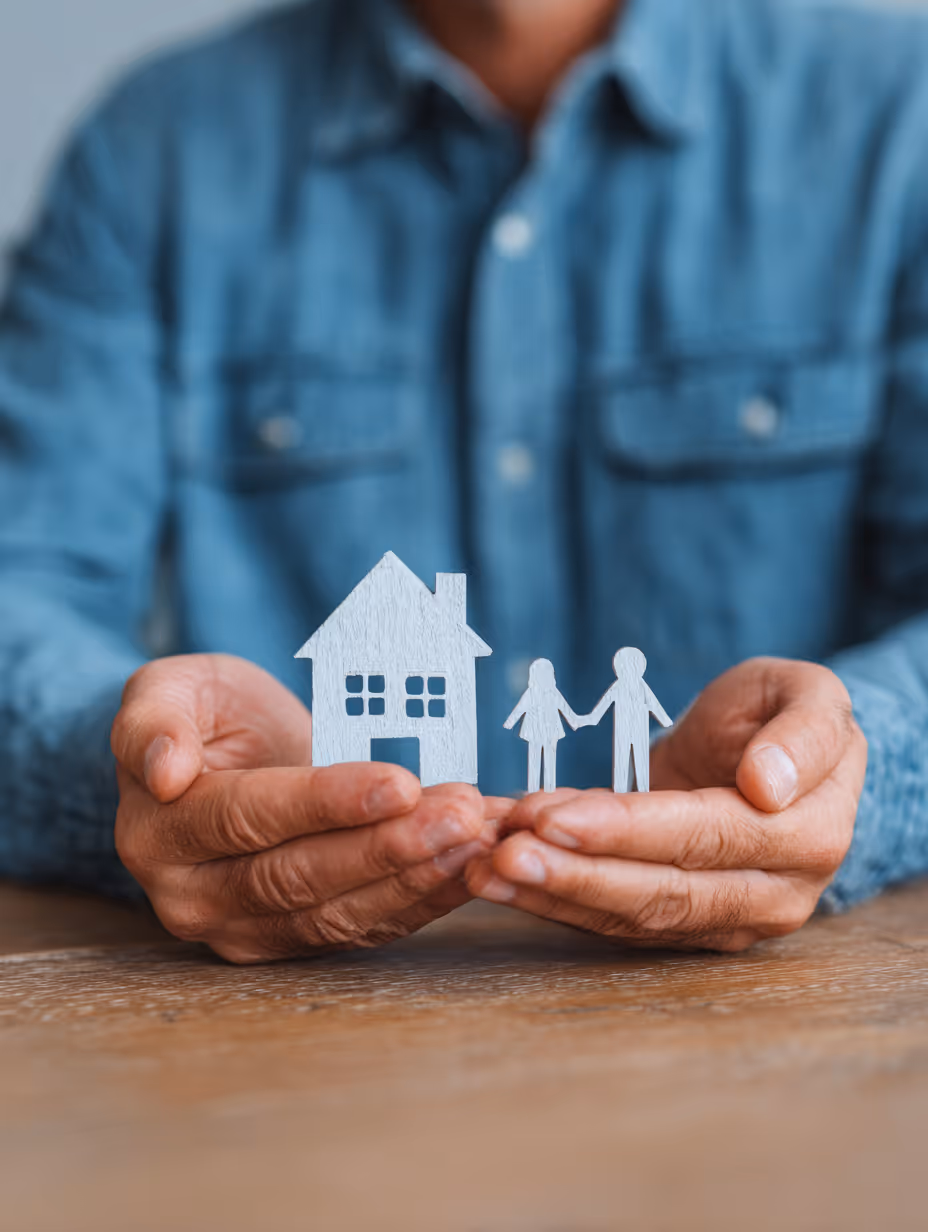 Person in blue shirt holding paper cutouts of a house and a man and woman holding hands.
