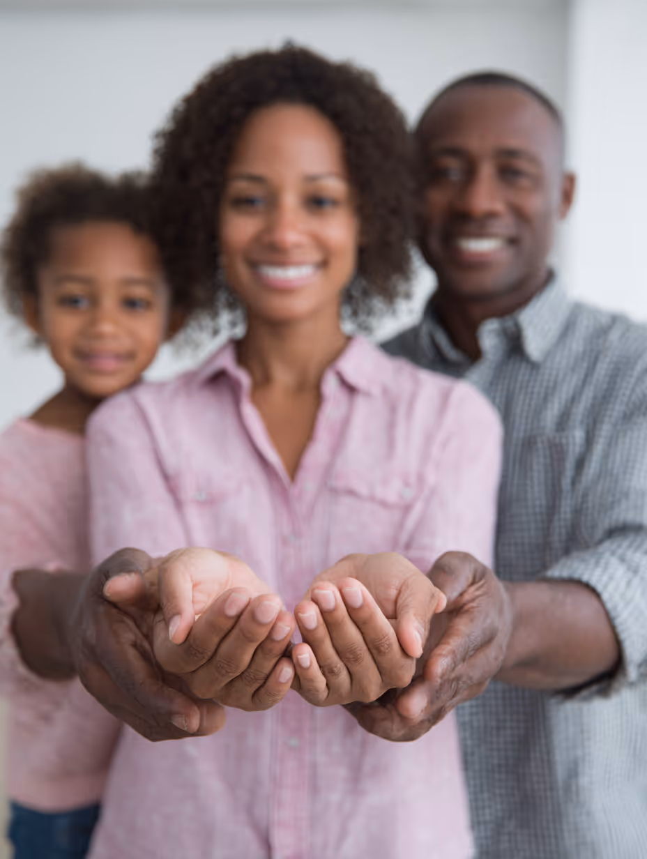 Smiling family of three standing with hands cupped together in front.
