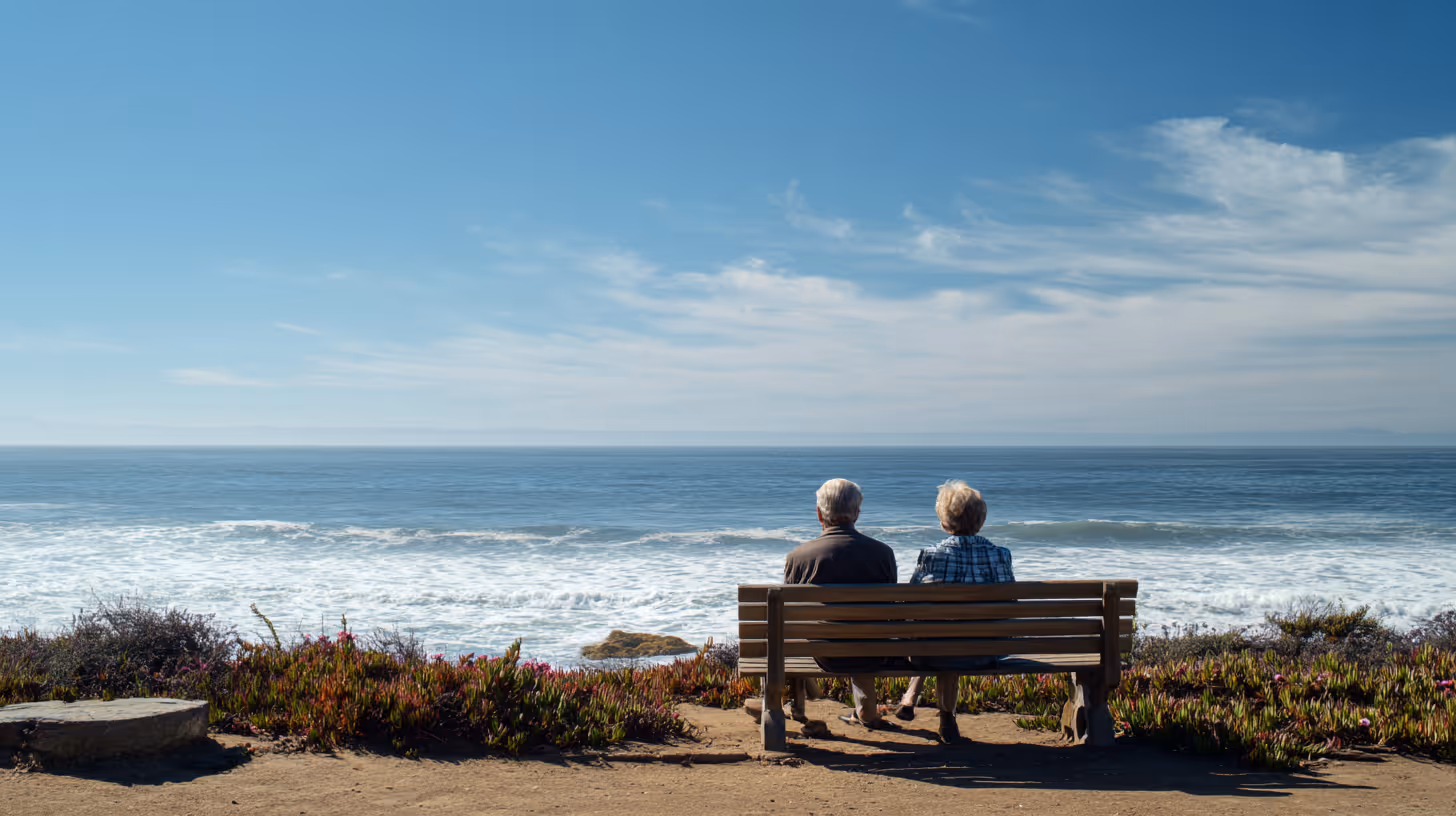 Elderly couple sitting on a bench overlooking the ocean on a clear day.
