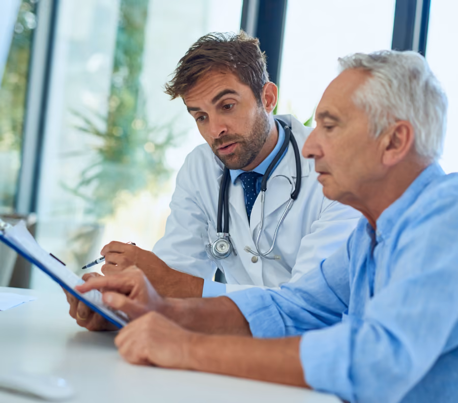 Male doctor with stethoscope discussing medical information with elderly male patient using clipboard.