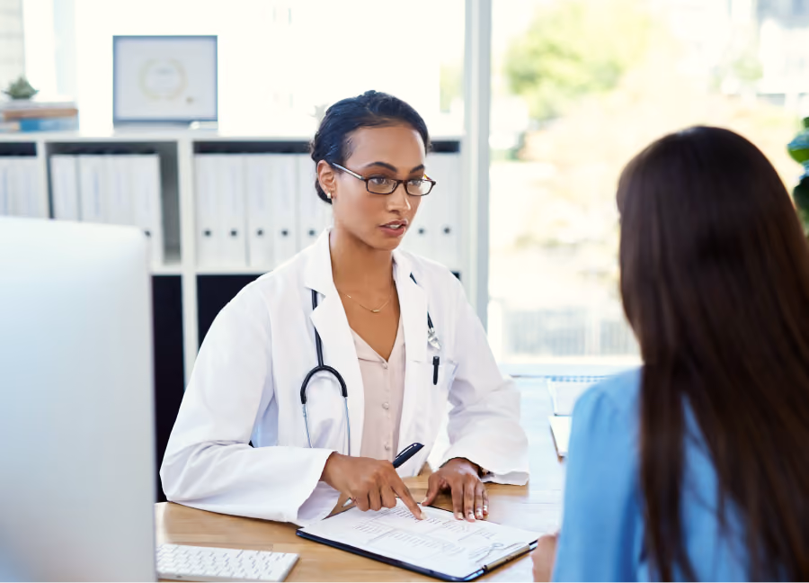 Female doctor wearing glasses and white coat discussing medical documents with a patient in an office.