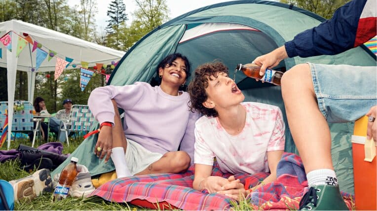 Zwei Personen mit Rivella auf einer Decke vor einem Zelt