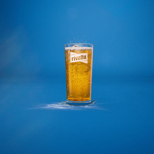 Gefülltes Rivella Blau Glas mit Eiswürfeln auf blauem Hintergrund