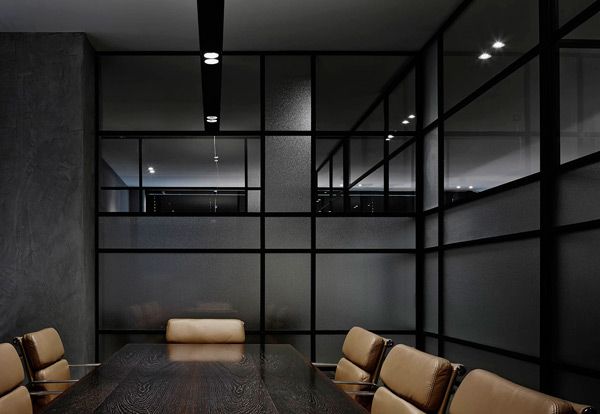 Modern conference room with a dark wooden table and tan leather chairs, surrounded by large glass partitions with black frames.