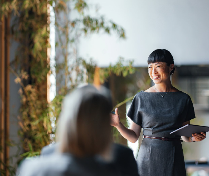 Smiling businesswoman with short black hair giving a presentation to colleagues in a modern office.