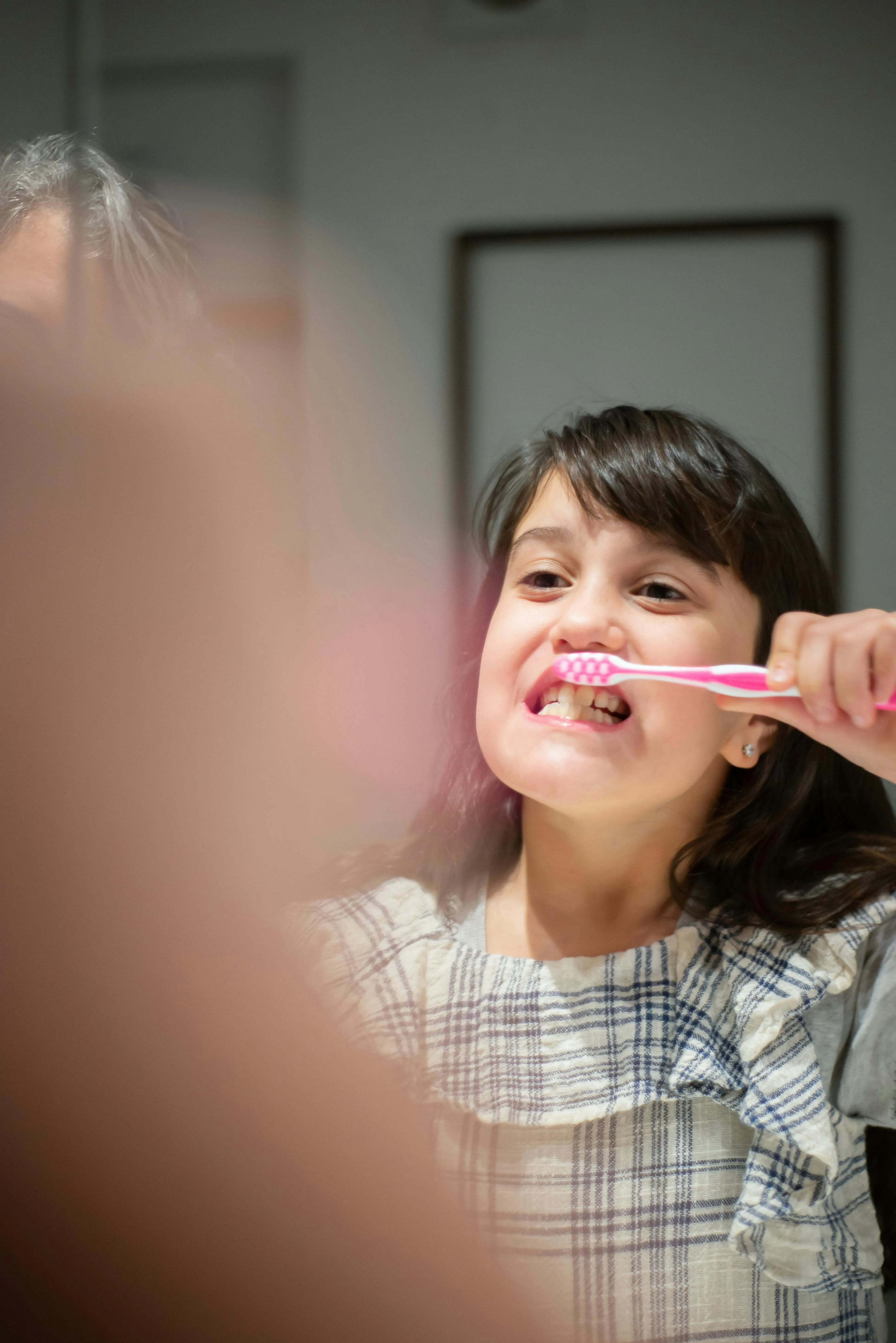 Young girl smiling and brushing her teeth with a pink toothbrush, representing the start of healthy dental habits in children