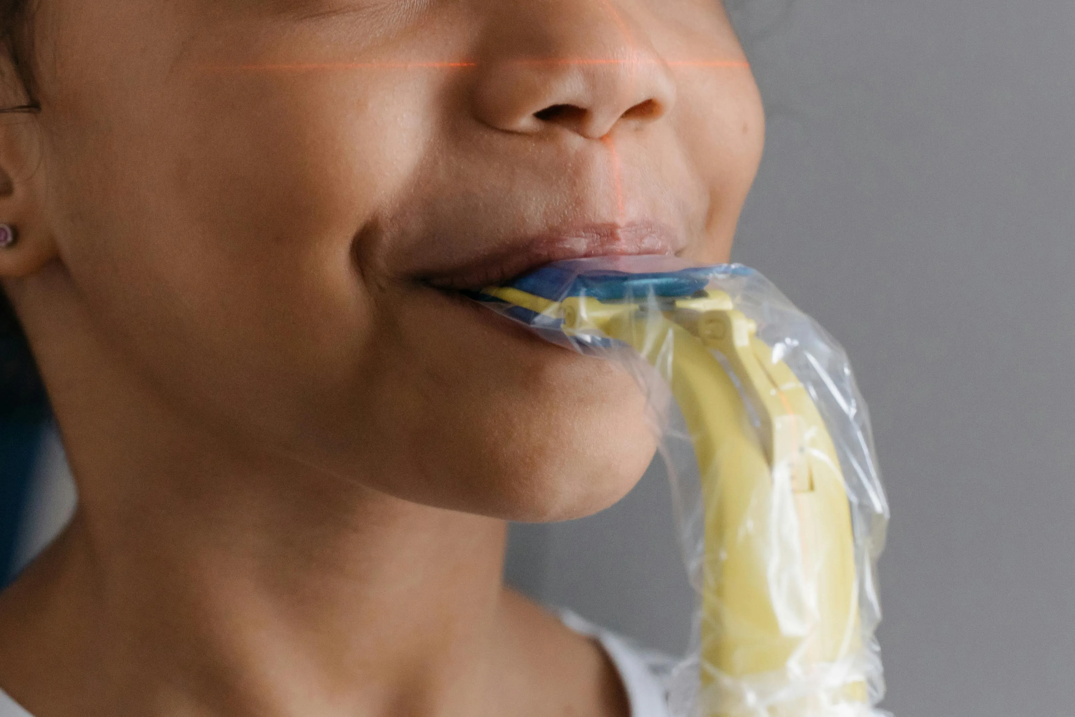 Close-up of a child's mouth with a yellow X-ray sensor positioned between the teeth to capture a digital dental X-ray