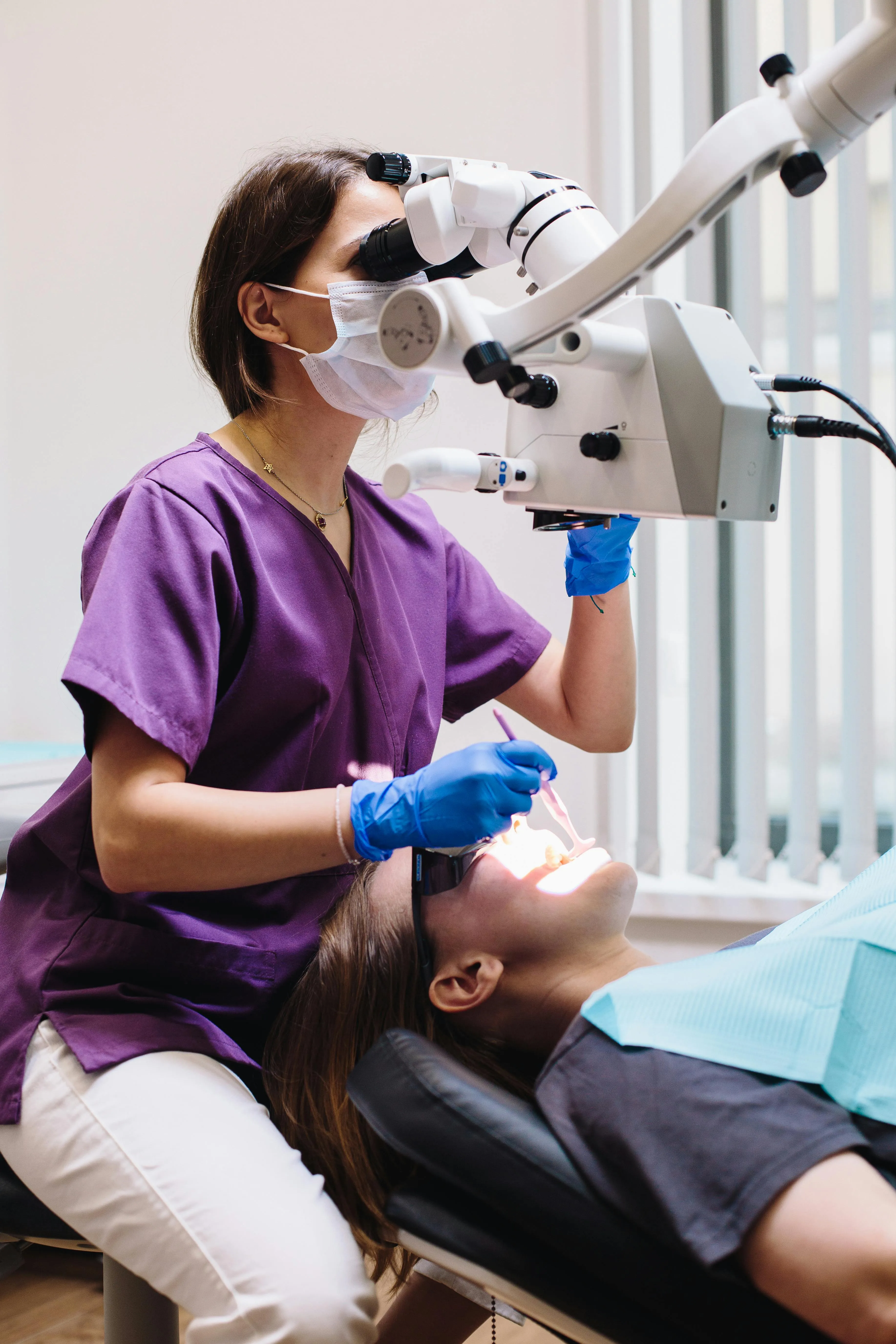 Dental professional in purple scrubs examining a patient's tooth to evaluate symptoms and determine whether root canal therapy is the appropriate treatment