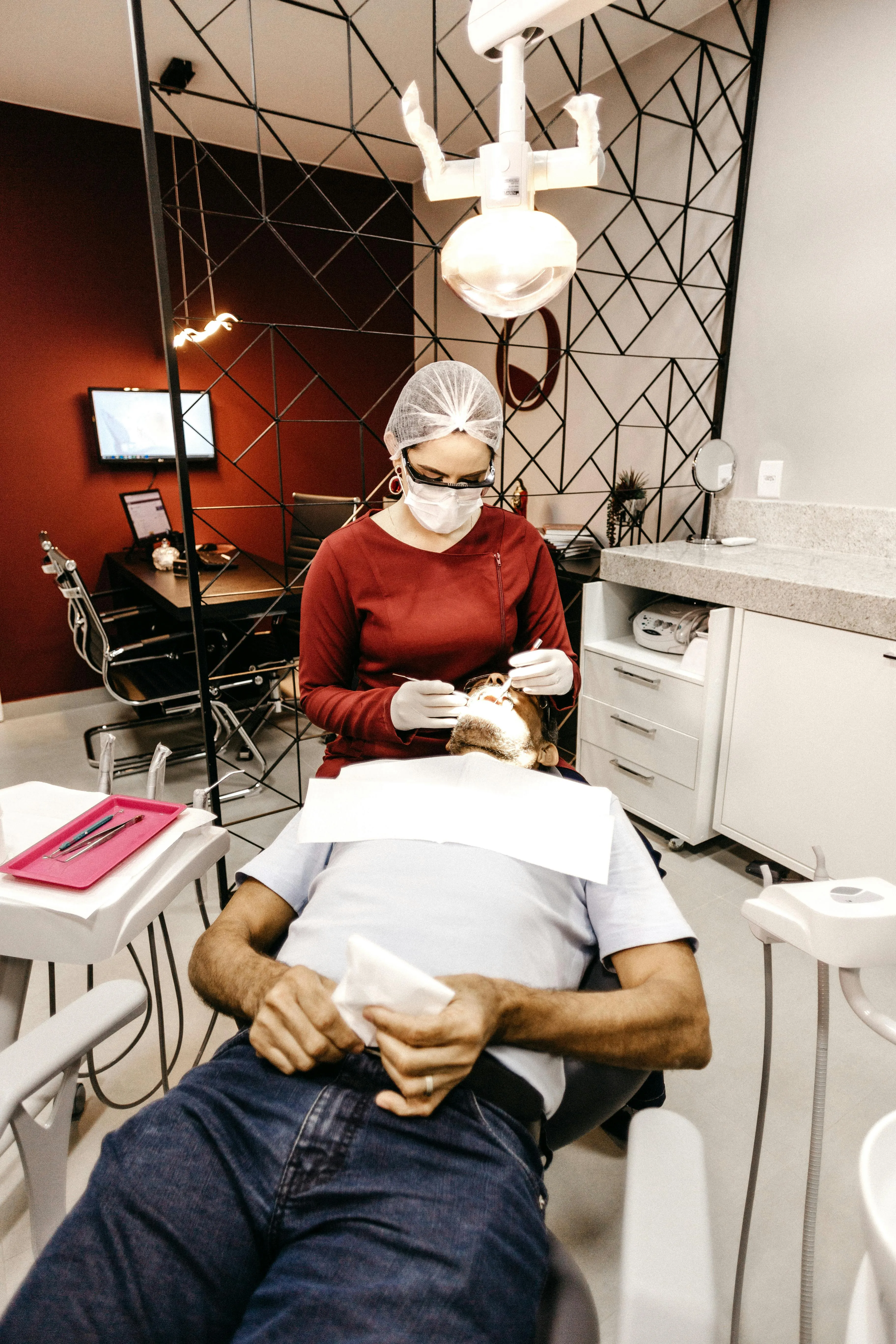 Dental professional in a red top and face mask performing an emergency exam on a patient to identify the source of pain or damage