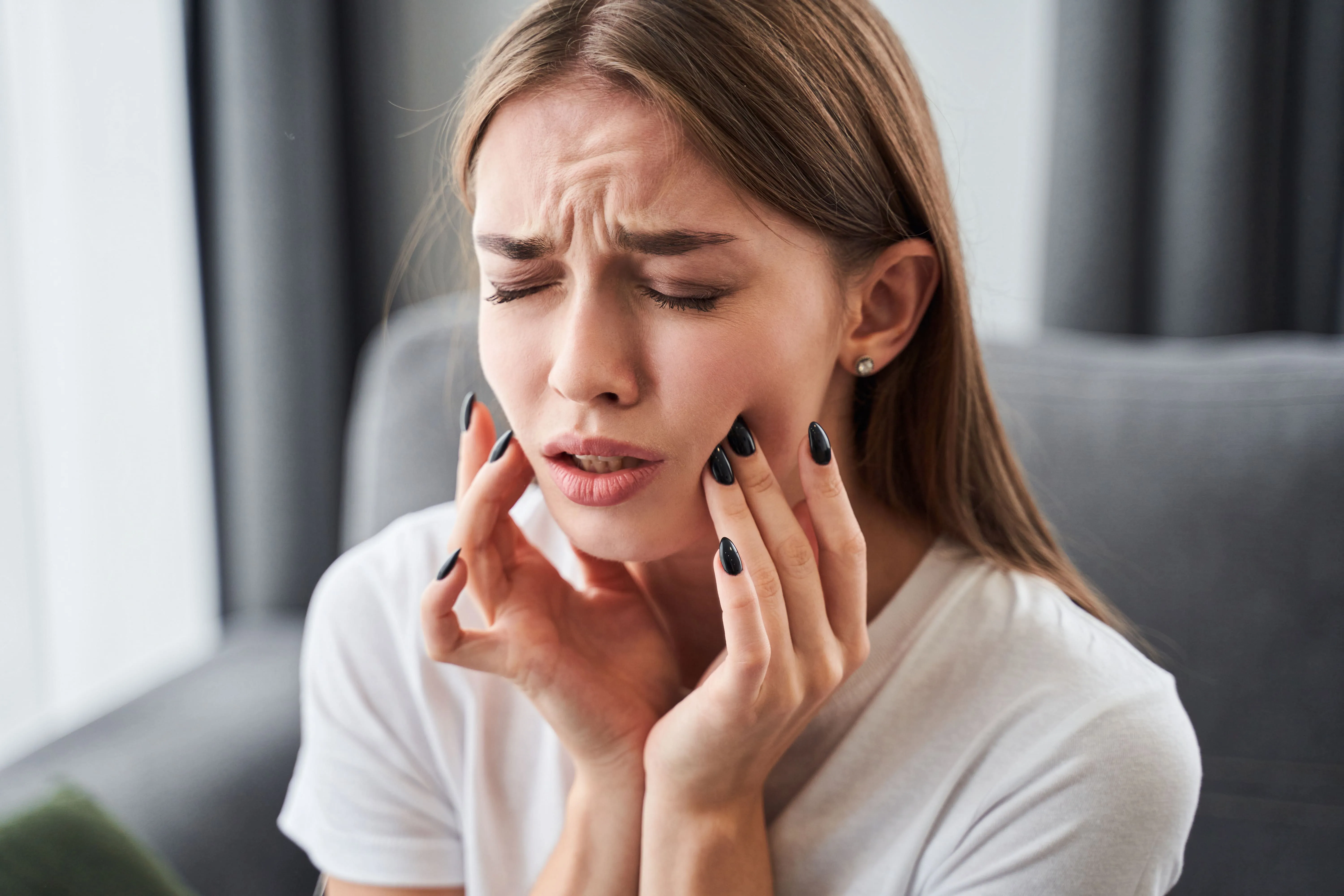 Woman with a pained expression holding her cheek and jaw, representing the severe or lingering tooth pain that may indicate the need for root canal therapy