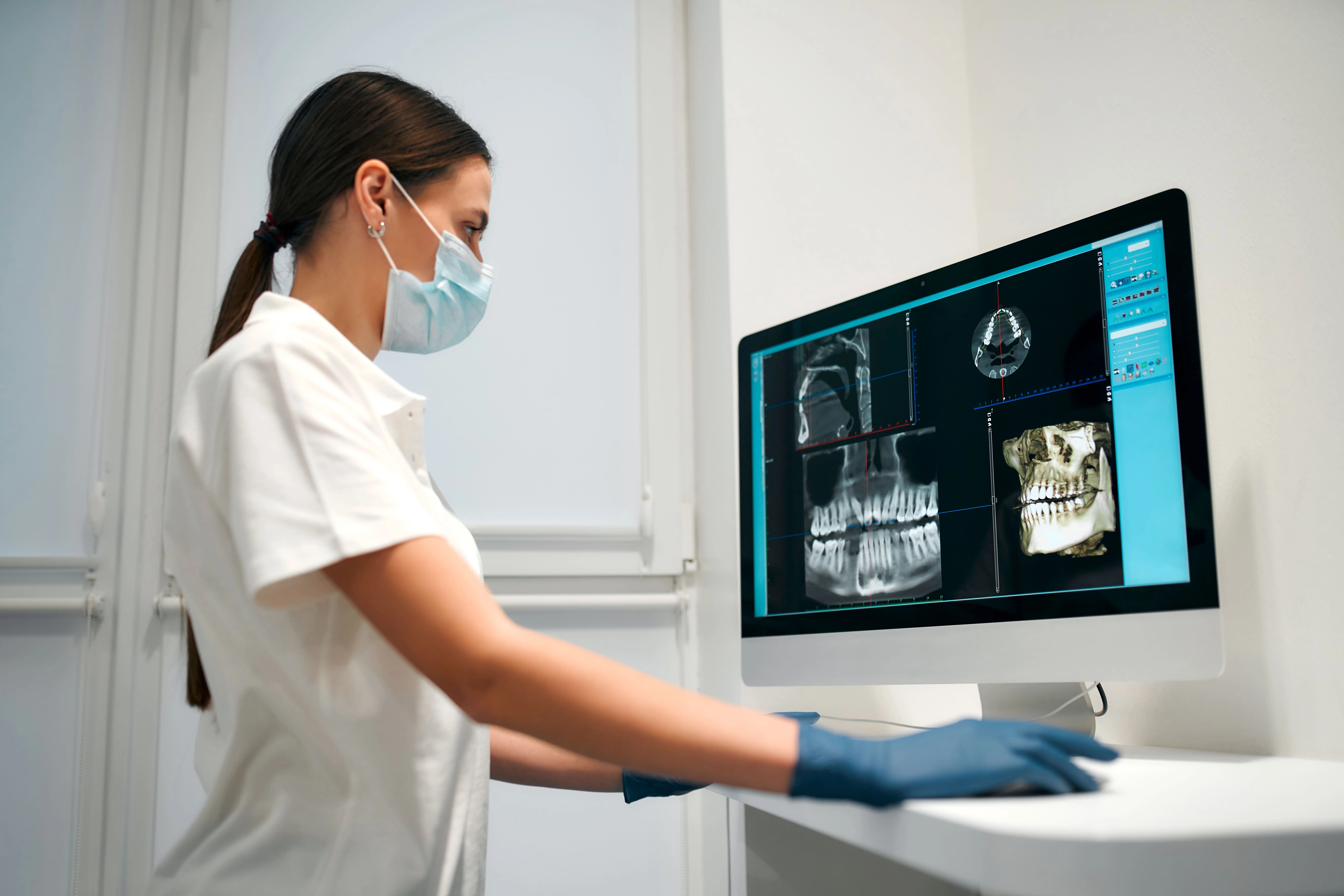 Dental clinician with a mask reviewing a dental X-ray on a monitor, representing the guided treatment planning process that maps the ideal implant position before surgery