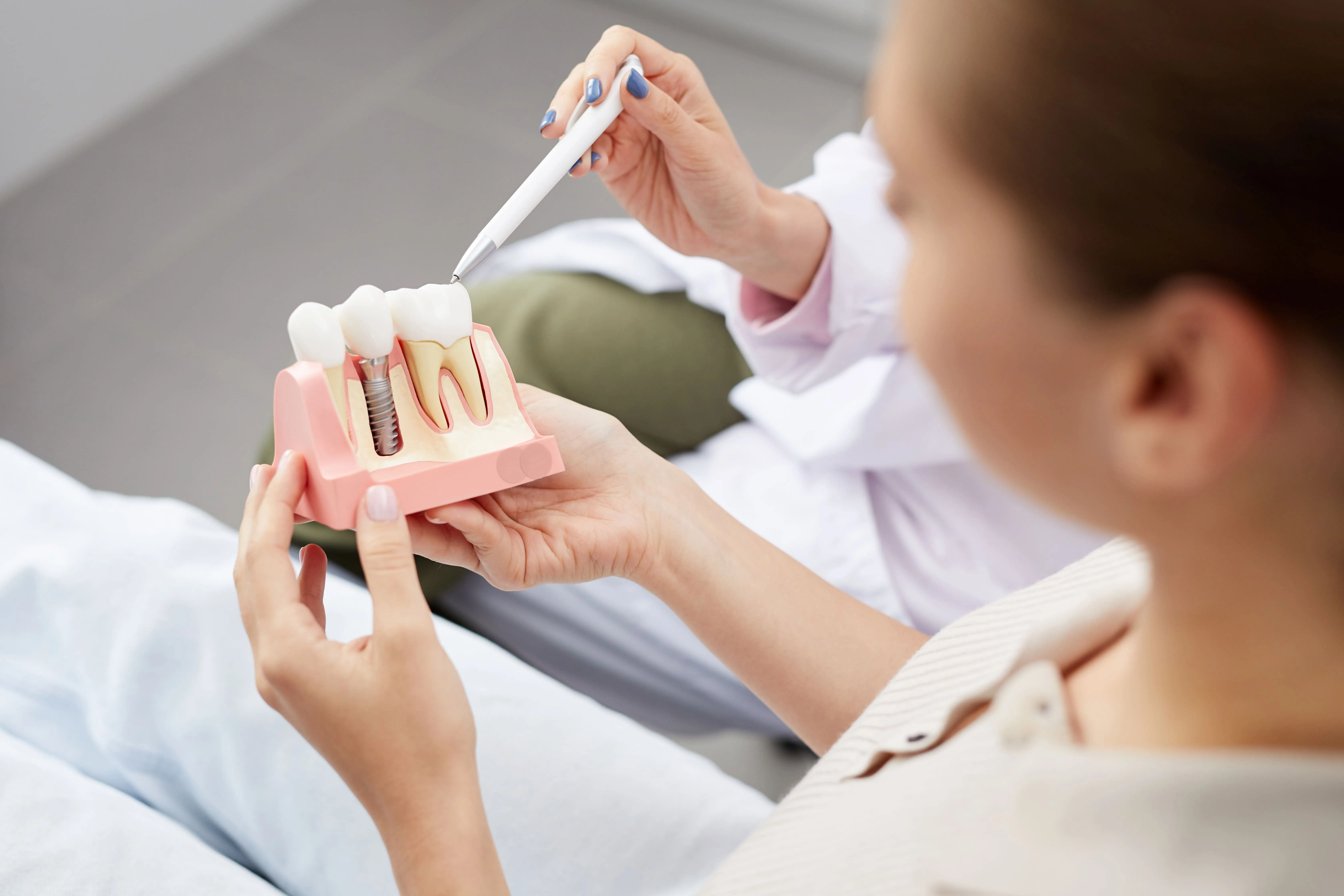 Dentist in San Juan Capistrano explaining a dental implant model to a patient, showing the titanium post and crown components