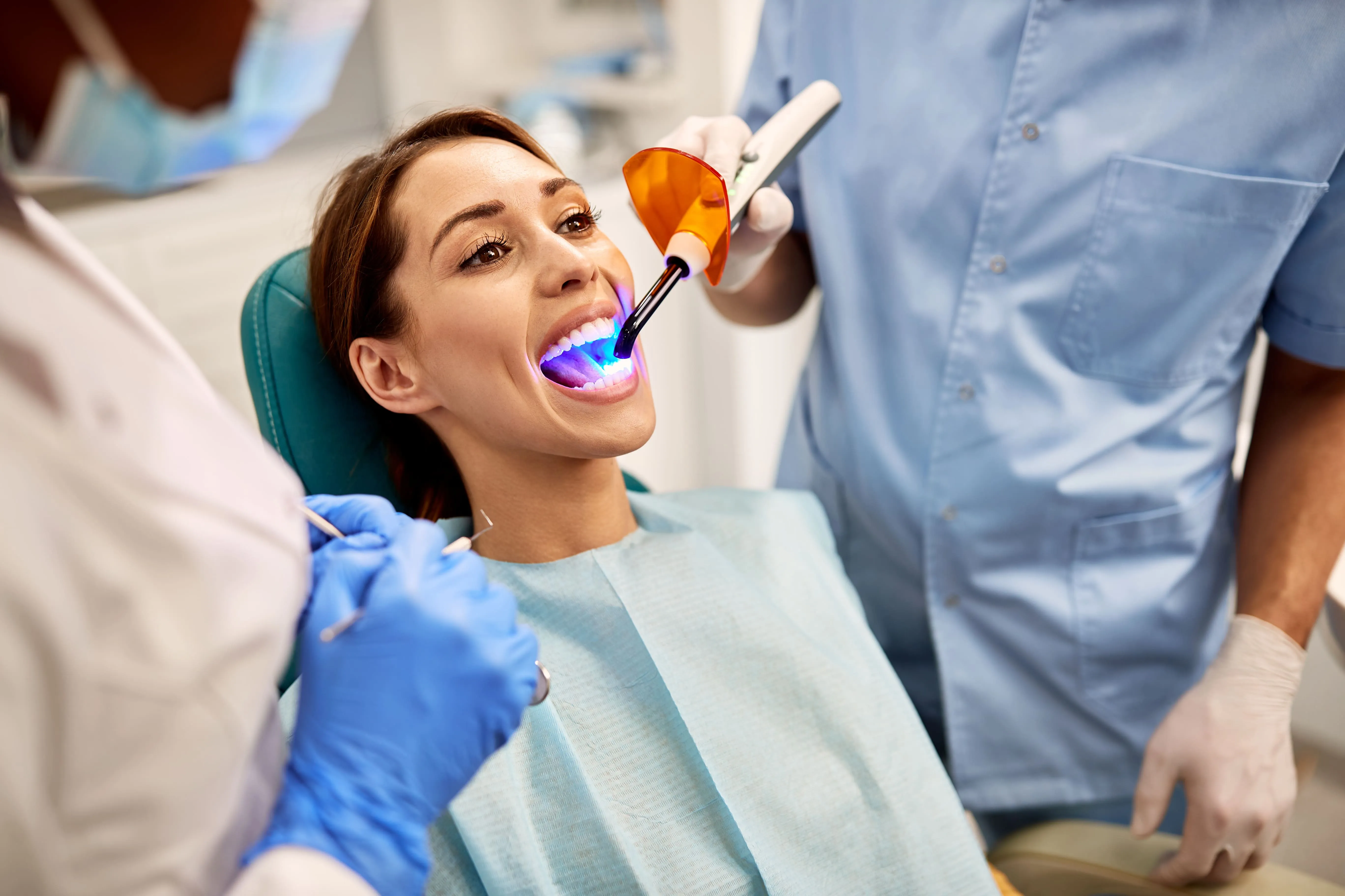 Woman in the dental chair with mouth open and a curing light applied, showing temporary protective treatment being placed to stabilize a damaged tooth