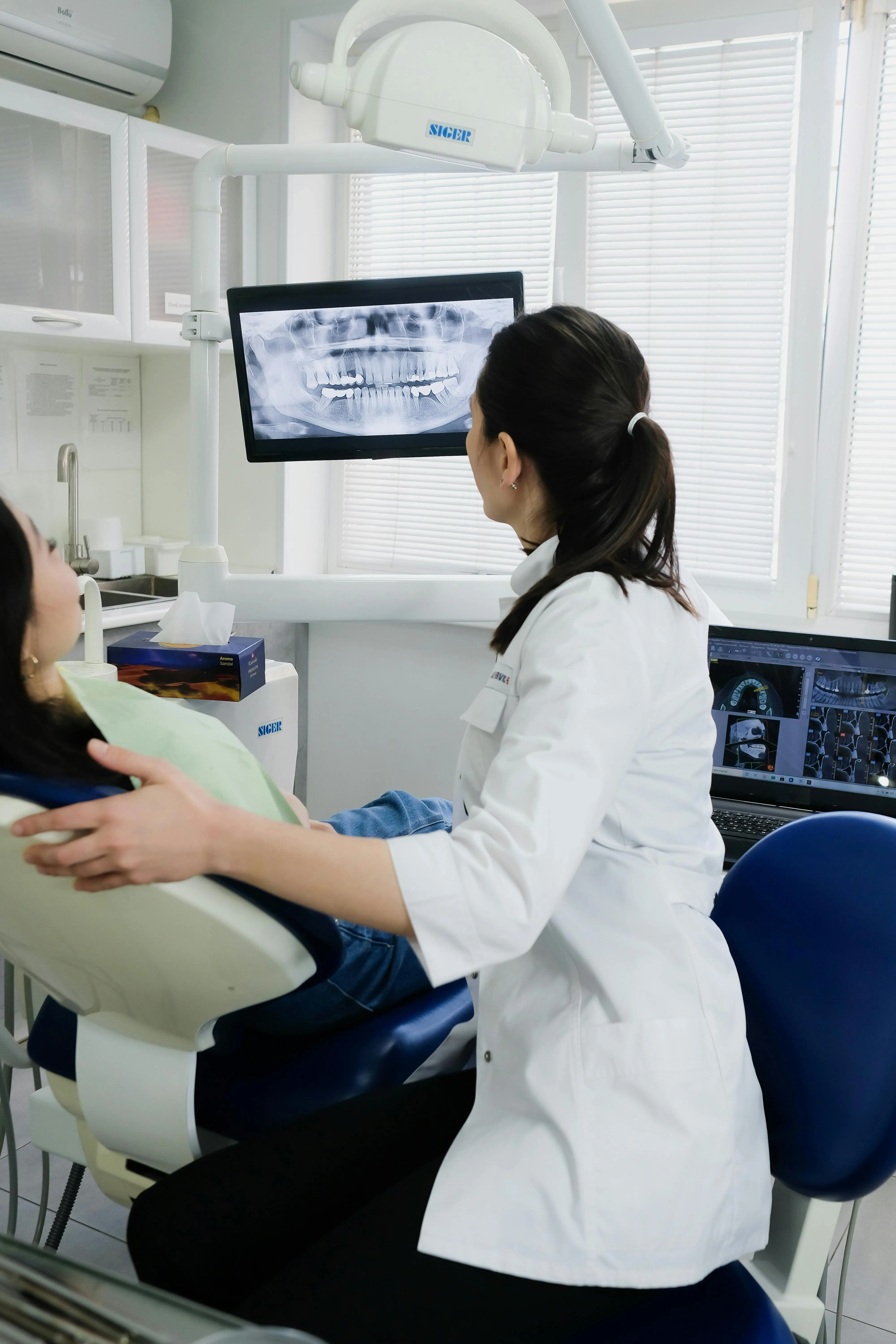 Dentist showing a patient's dental X-ray on a monitor in a clinic room.