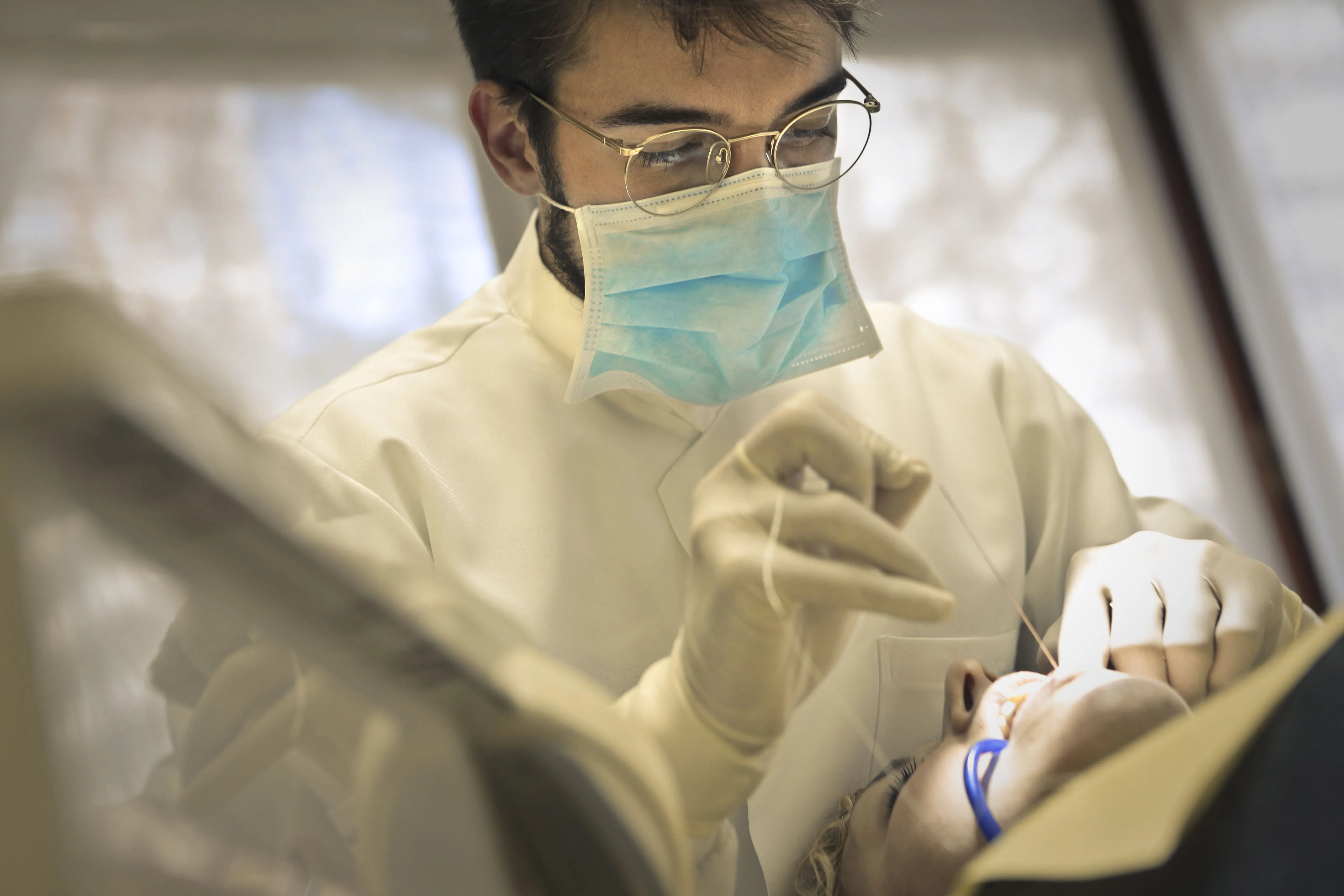 Dentist wearing mask and gloves performing dental work on patient lying back in chair.