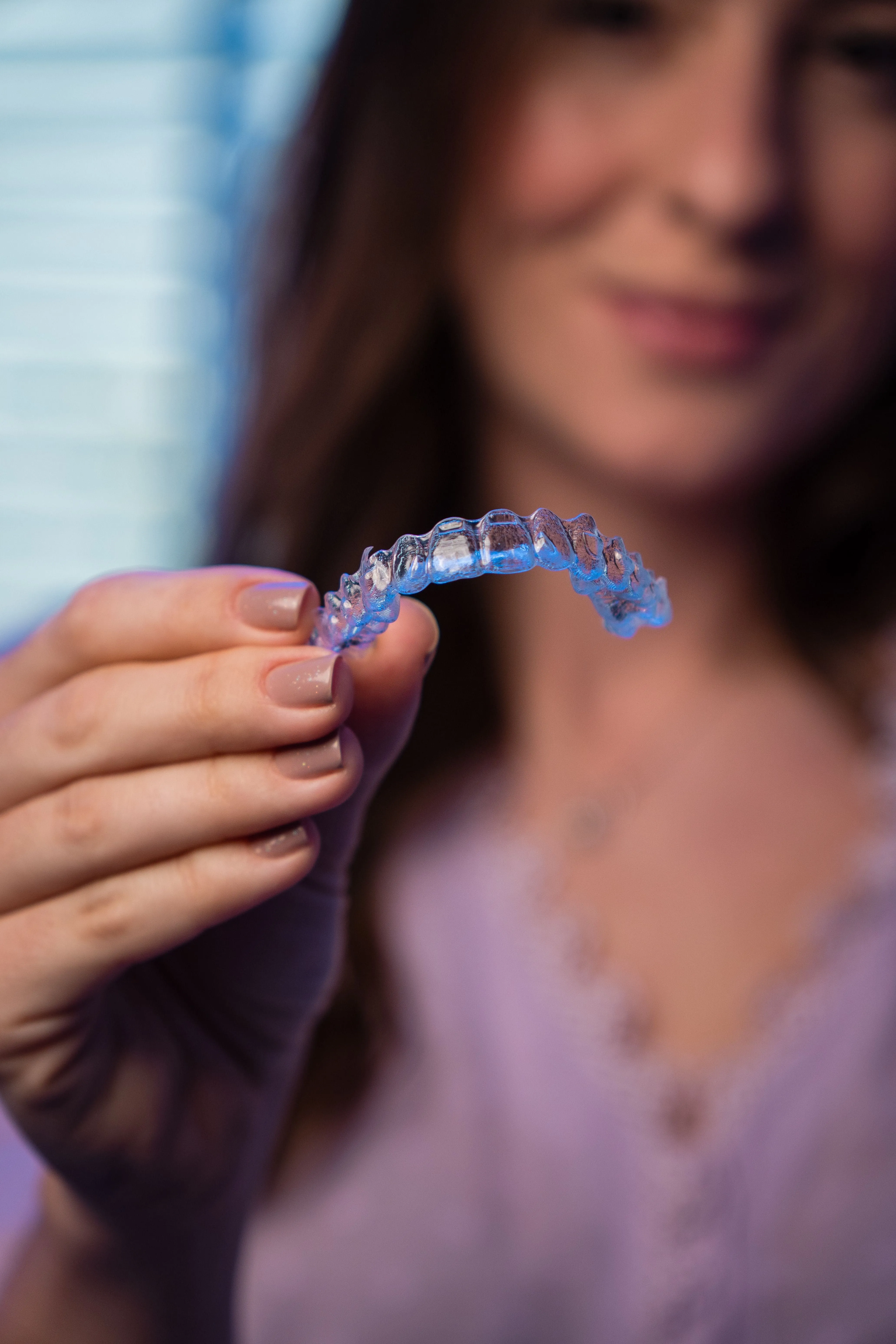 Smiling woman holding a clear Invisalign aligner tray up to her teeth, representing the discreet and comfortable orthodontic treatment available through Invisalign® at Ortega Cottage Dentistry in San Juan Capistrano