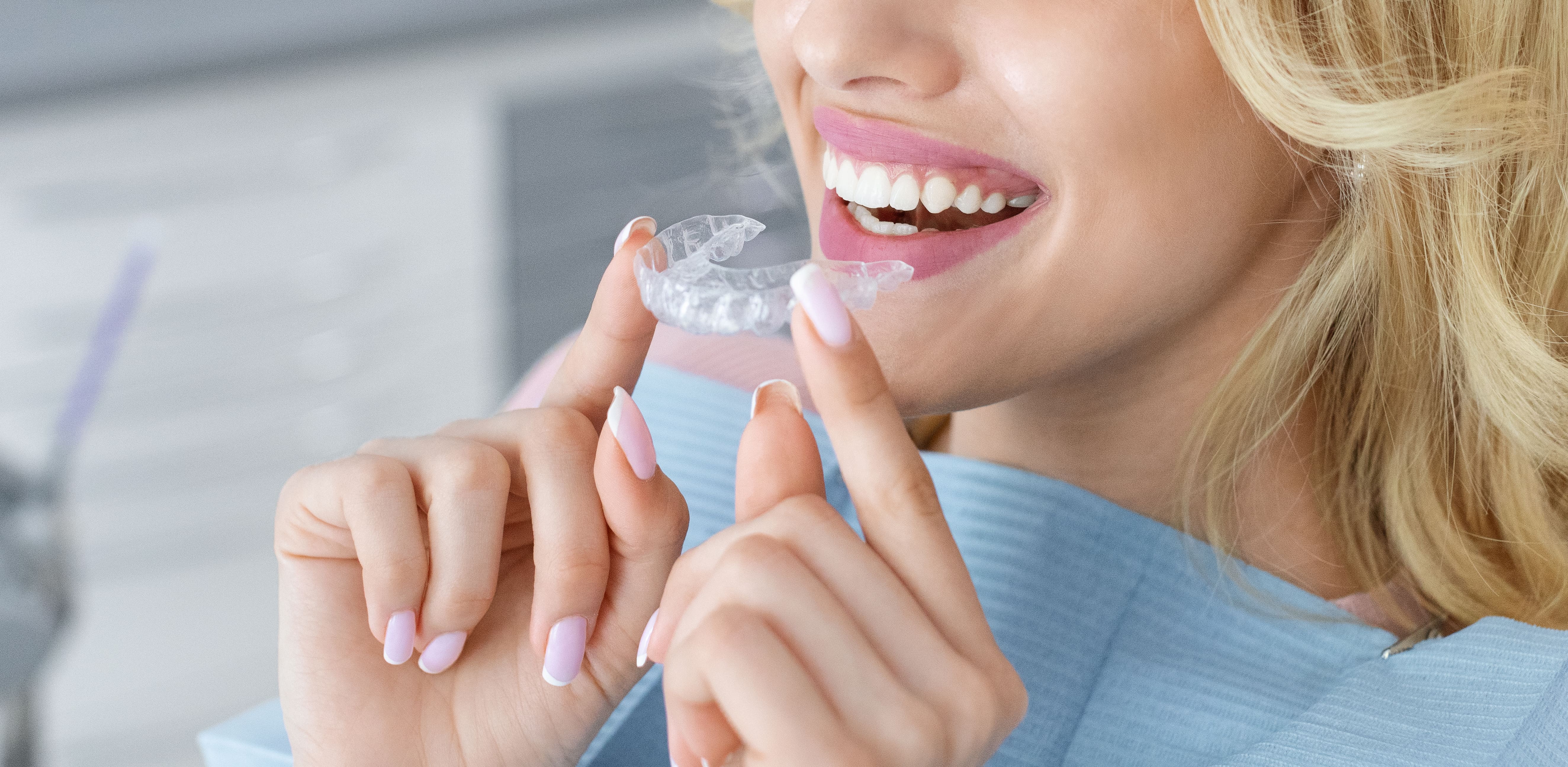 Smiling woman holding a clear Invisalign aligner tray up to her teeth, representing the discreet and comfortable orthodontic treatment available through Invisalign® at Ortega Cottage Dentistry in San Juan Capistrano